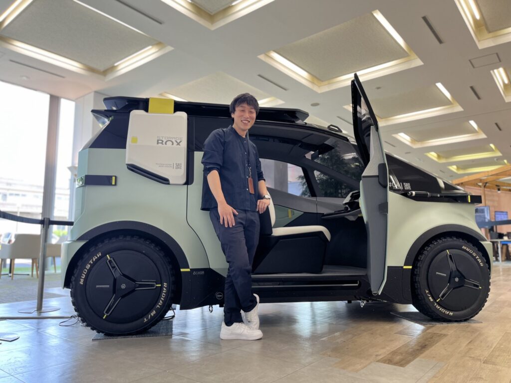 上海のEV車の前でポーズする黄峻さん